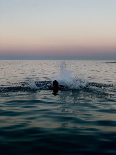 Silhouette person swimming in sea against sky during sunset
