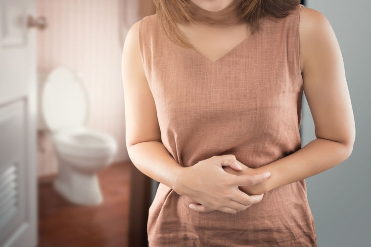 Midsection of woman with stomachache standing against toilet