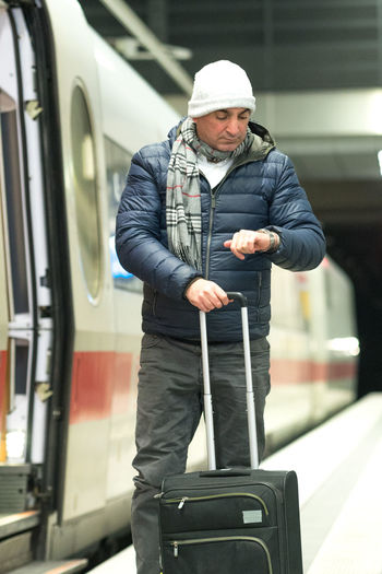 Man checking time while standing with luggage on railroad station platform