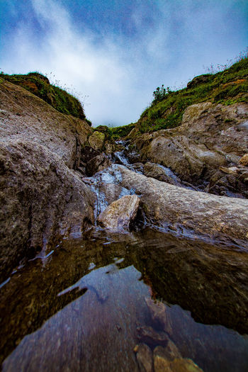 Scenic view of water flowing through rocks against sky
