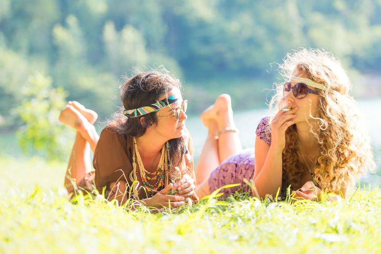 Female friends smoking cigarette while lying on land
