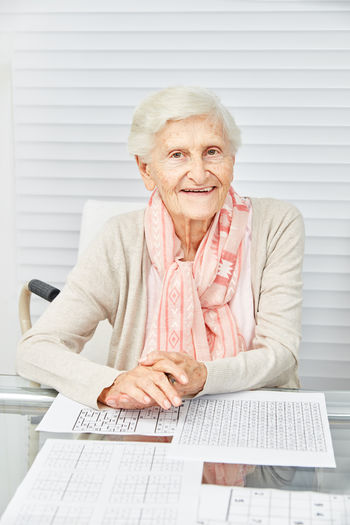Portrait of smiling senior woman with crossword puzzle sitting at nursing home
