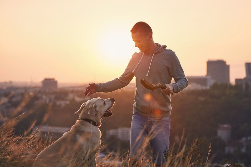 Woman with dog standing against sky during sunset