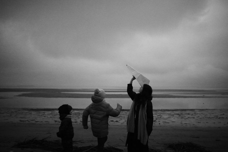 Rear view of children on beach against sky