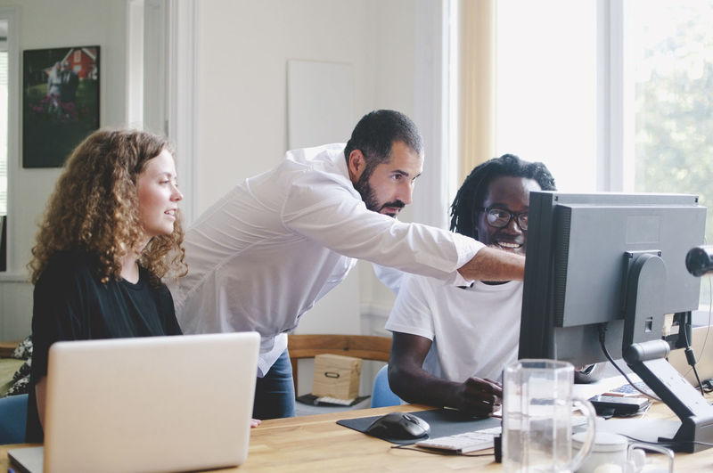 Multi-ethnic business people discussing over computer at table in creative office