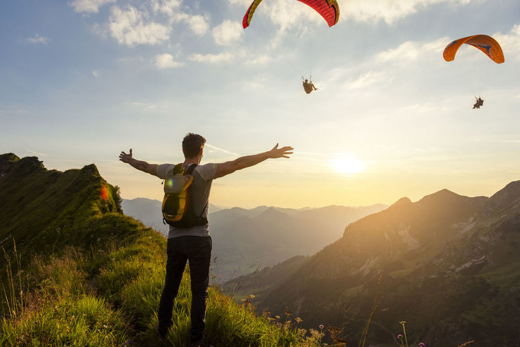 Germany, bavaria, oberstdorf, man on a hike in the mountains at sunset with paraglider in background