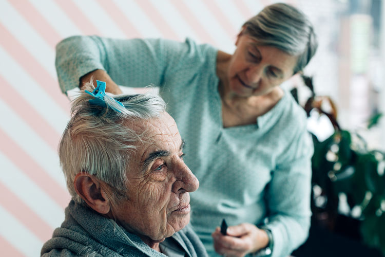 Elderly man receives home barber service - elderly wife cuts hair to old husband