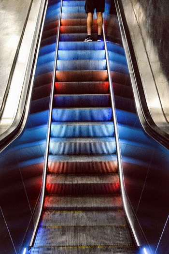 Low section of man standing on illuminated escalator