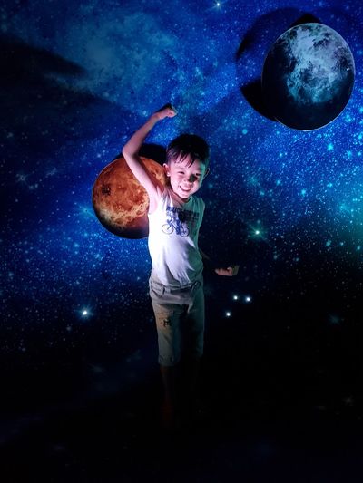 Digital composite image of boy standing against star field at night