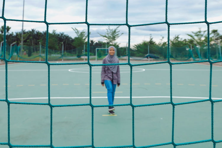 Teenage girl wearing hijab walking on playing field seen from net