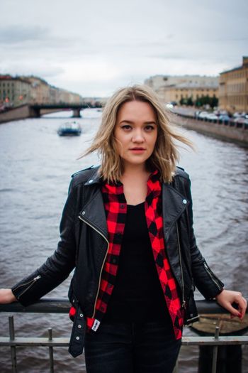 Portrait of young woman against river in city