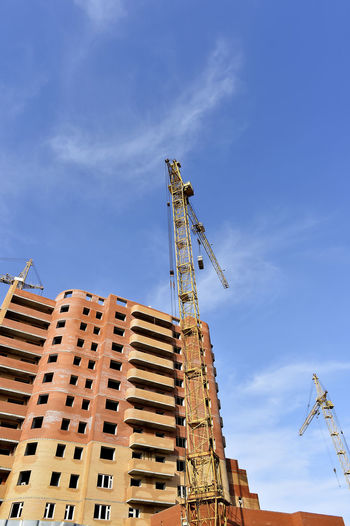 Low angle view of crane by buildings against blue sky