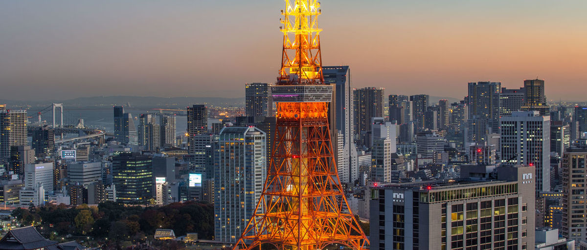 Illuminated tokyo tower amidst city against clear sky during sunset