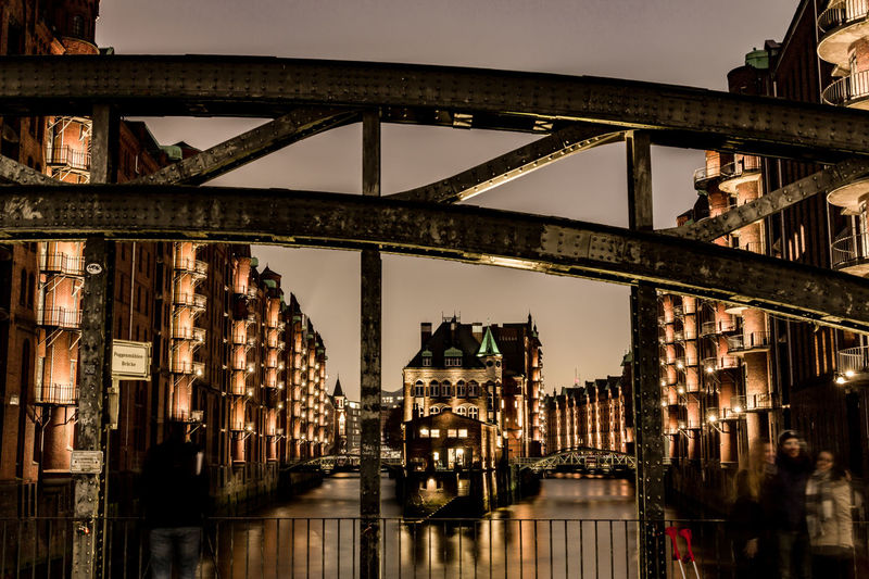 Illuminated old buildings on canal against sky at speicherstadt