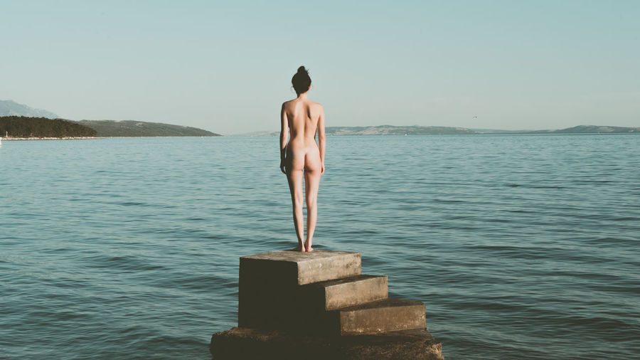 Naked woman standing on steps at beach against sky