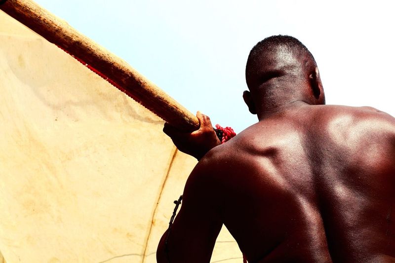 Low angle view of shirtless man holding wood against sky