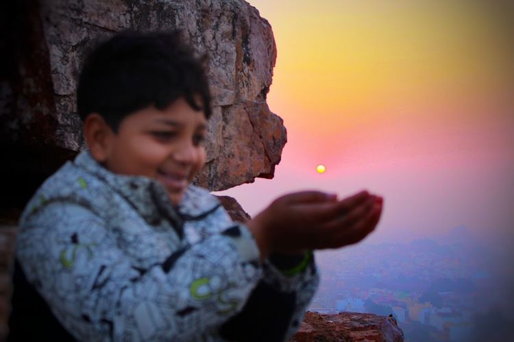 Close-up of boy cupping hands against sky during sunset