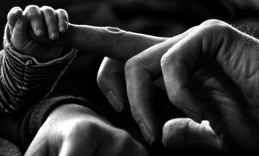 Cropped image of baby holding parent finger at home