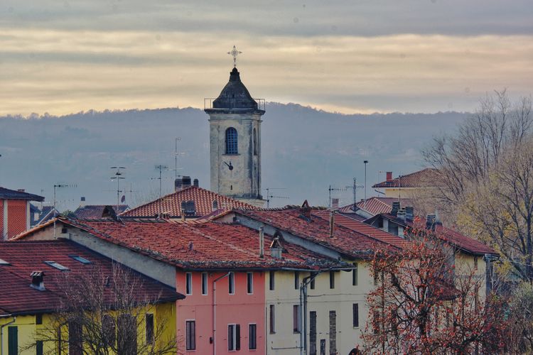 A bell tower in a rural town, under a cloud sky, in piedmont, italy