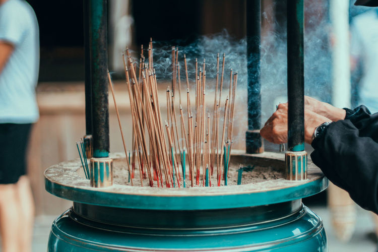Cropped hands of man placing burning incense in container at temple