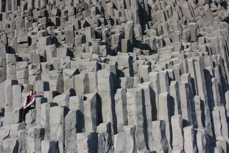 Low angle view of woman sitting on basalt columns at vik