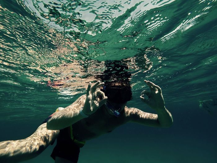 Shirtless man gesturing while swimming in sea