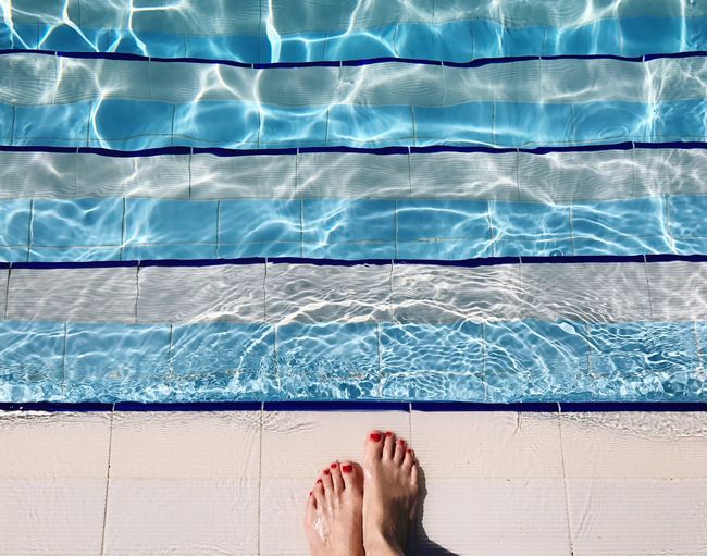 Low section of woman standing at poolside during sunny day