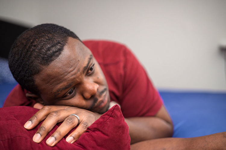 Young depressed or anxious african american man in bedroom at home sitting