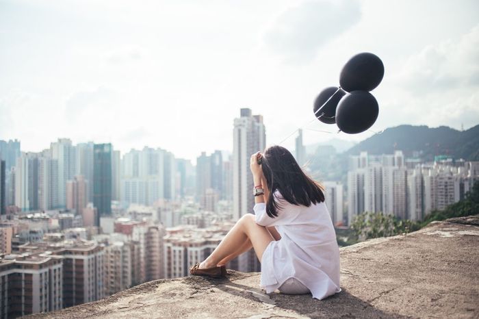 Woman holding black balloons looking at cityscape
