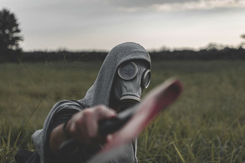 Man wearing gas mask holding axe on land