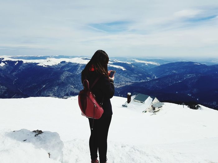 Woman using mobile phone while standing on snowcapped mountain against sky