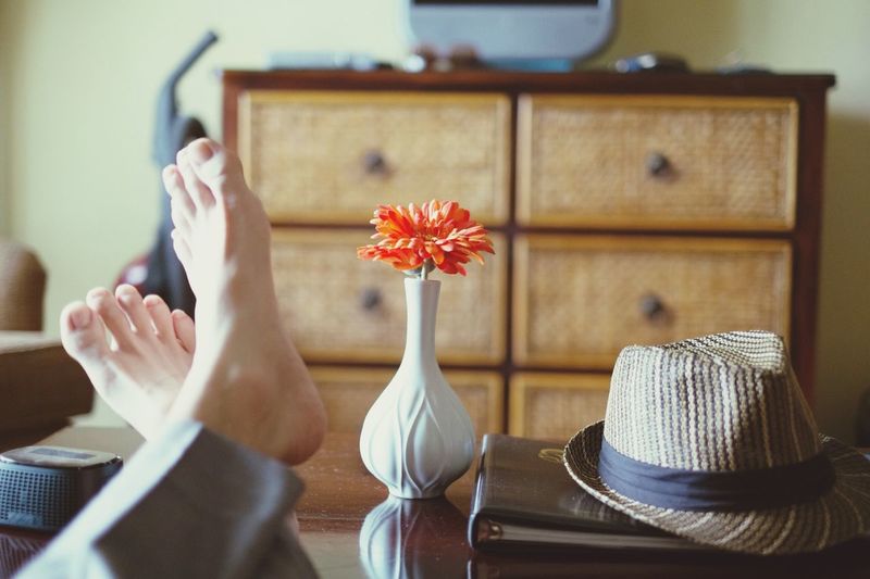 Close-up of persons feet resting on coffee table near vase and hat