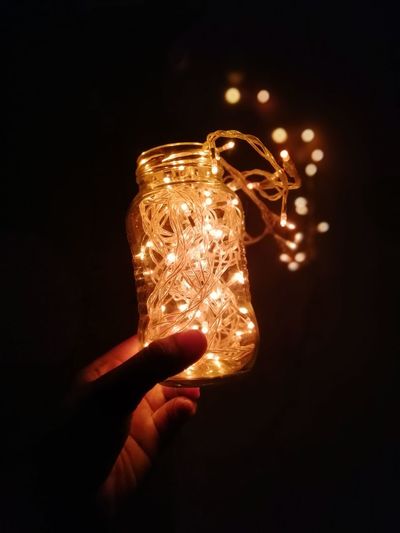 Close-up of hand holding illuminated light against black background