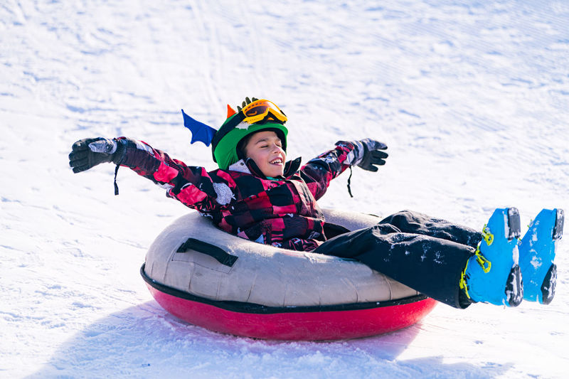Full length of boy over inflatable raft on snow