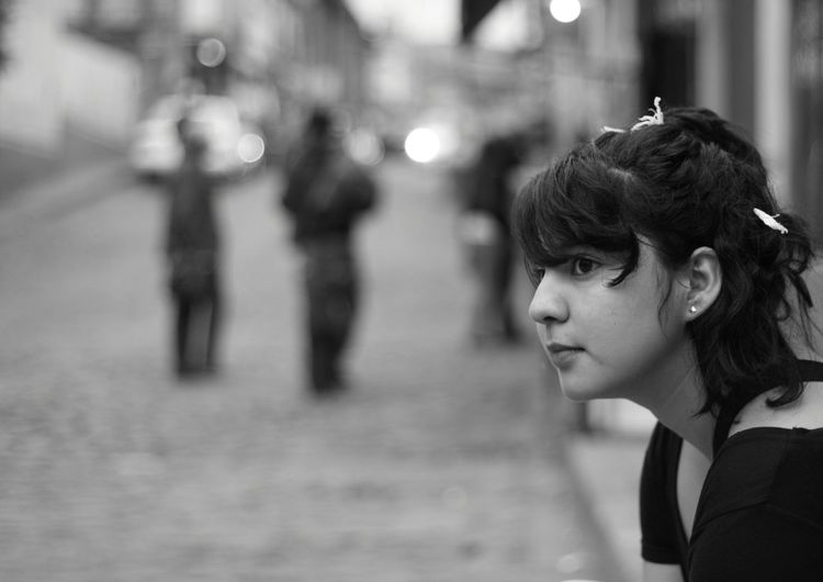 Close-up of young woman looking away while standing on street in city