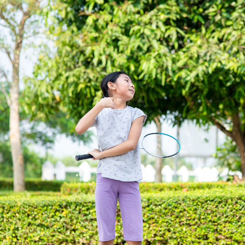 Girl holding badminton racket while standing by plants