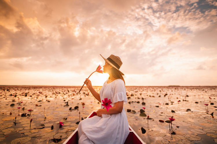 Woman sitting on boat holding flower against sky