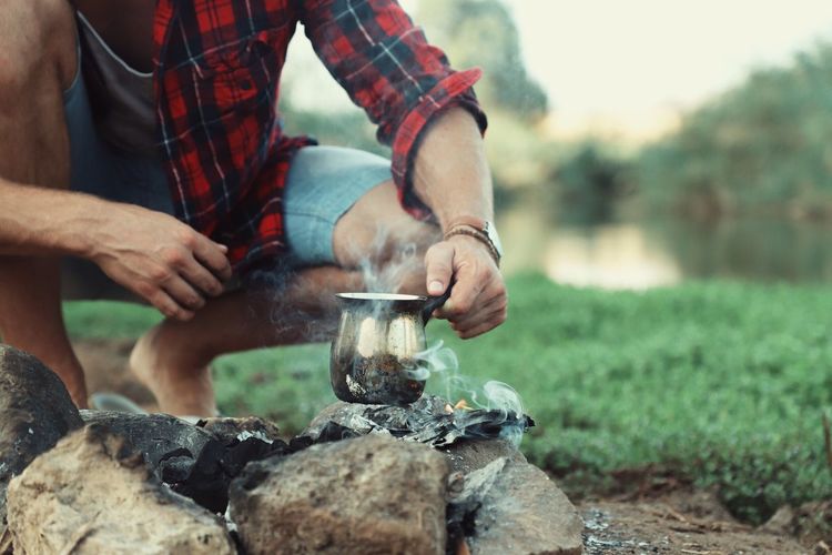 Midsection of man boiling drinking water on campfire