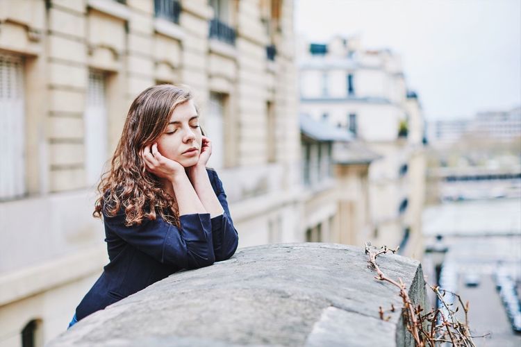 Young woman with eyes closed leaning on concrete wall