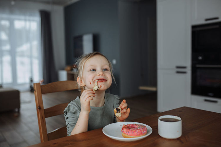 Little girl 5 years old in the kitchen eating a chocolate donut with tea