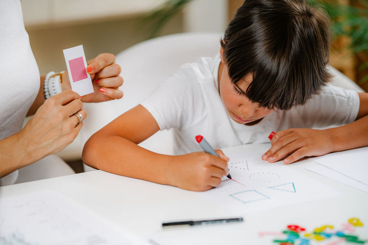 Child drawing shapes in a preschooler assessment test. psychologist helping him.