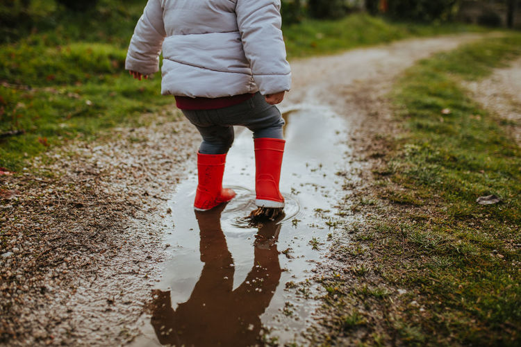 Low section of baby girl standing on puddle during rainy season