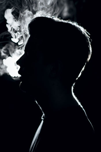 Close-up portrait of man smoking cigarette against black background