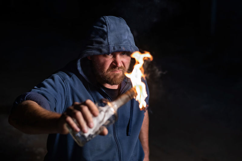 Man wearing hood holding burning bottle against black background