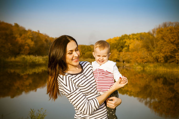 Mother holding daughter at lake during sunny day