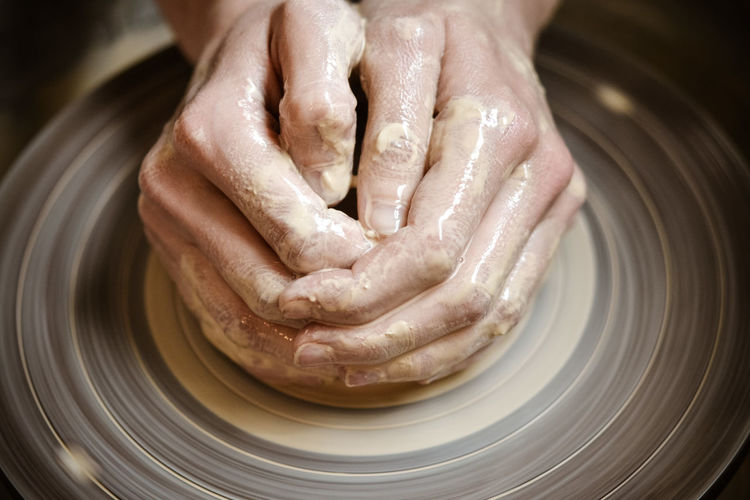 Master potter folded together hands sculpts a clay product on a potter's wheel close-up. 