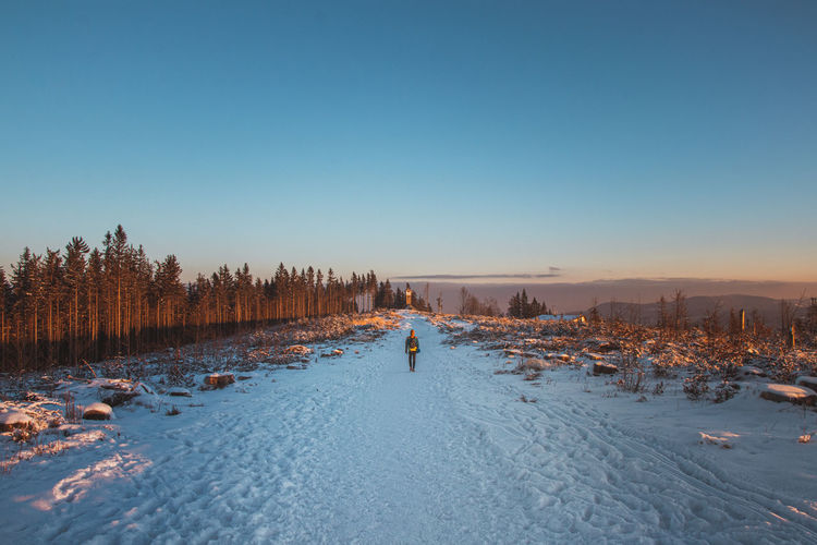 Man in winter clothes walking through a snowy road and a landscape without trees at sunrise
