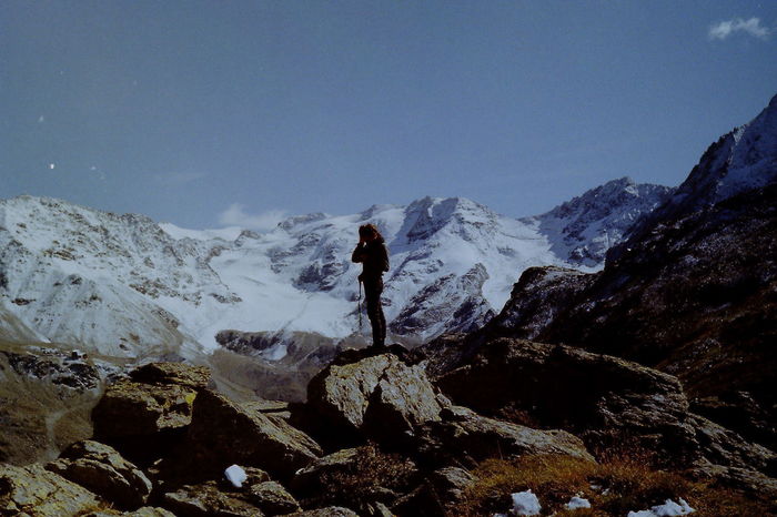 MAN STANDING ON ROCKS AGAINST MOUNTAINS