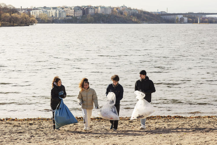 Young male and female environmentalists with collected microplastics walking against lake
