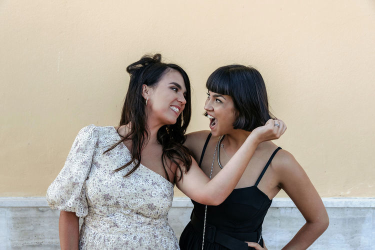 Portrait of two attractive women wearing stylish dresses, pulling each other's hair